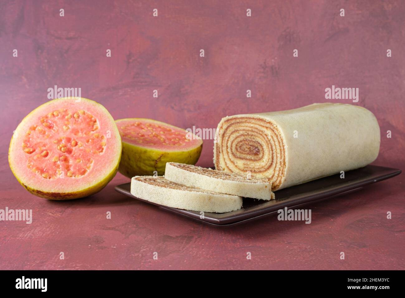 Bolo de rolo in Scheiben geschnitten auf einer braunen Platte, neben einer Guave (Seitenansicht). Stockfoto