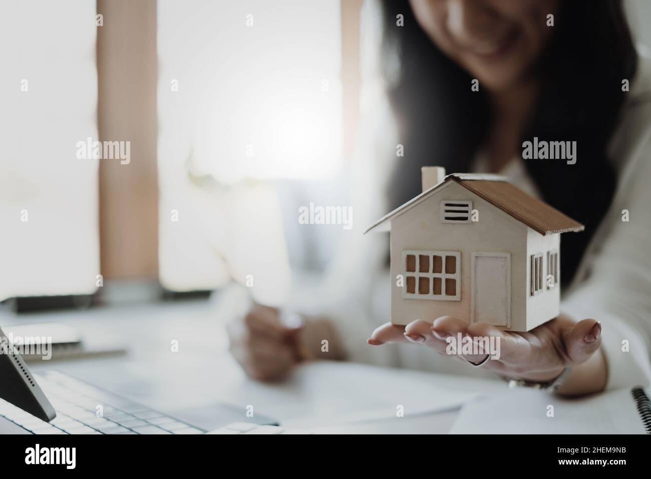 Eine Frau, die das Hausmodell hält und überprüft.Immobilienhaus-Bewertung und Inspektions- und Versicherungskonzept. Stockfoto
