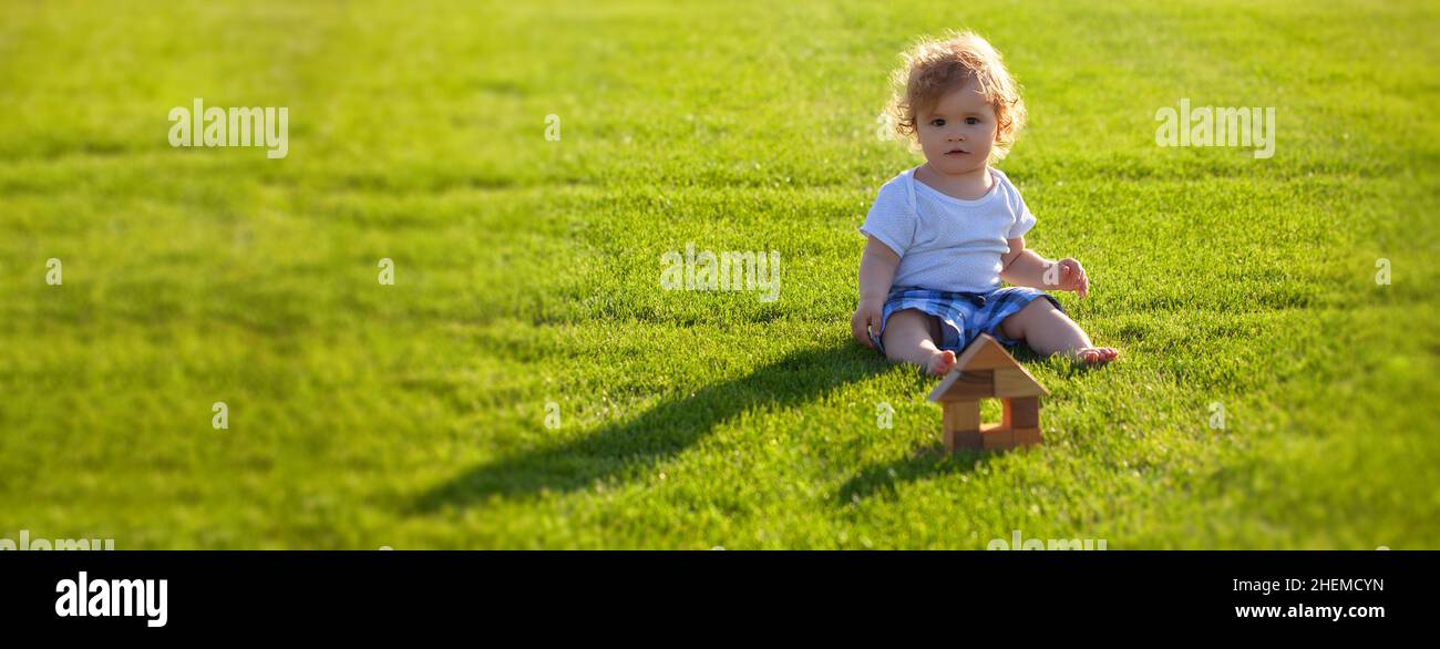 Banner mit Feder Kindergesicht. Versicherung für Kinder. Baby spielen im grünen Gras. Warme Frühlingszeit im Park. Stockfoto