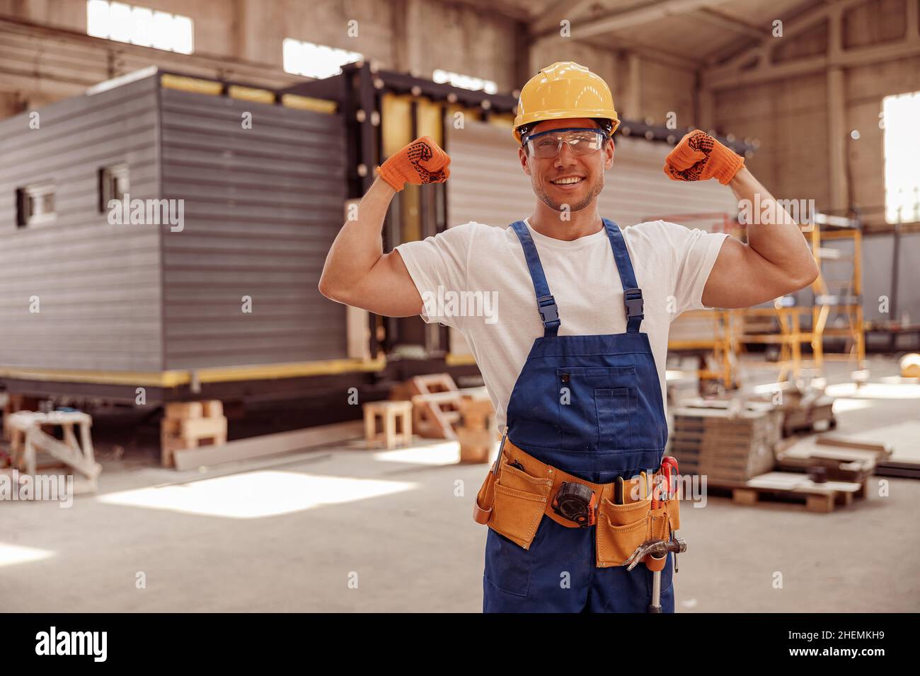 Fröhlicher Arbeiter, der seine starken muskulösen Arme demonstrierte Stockfoto