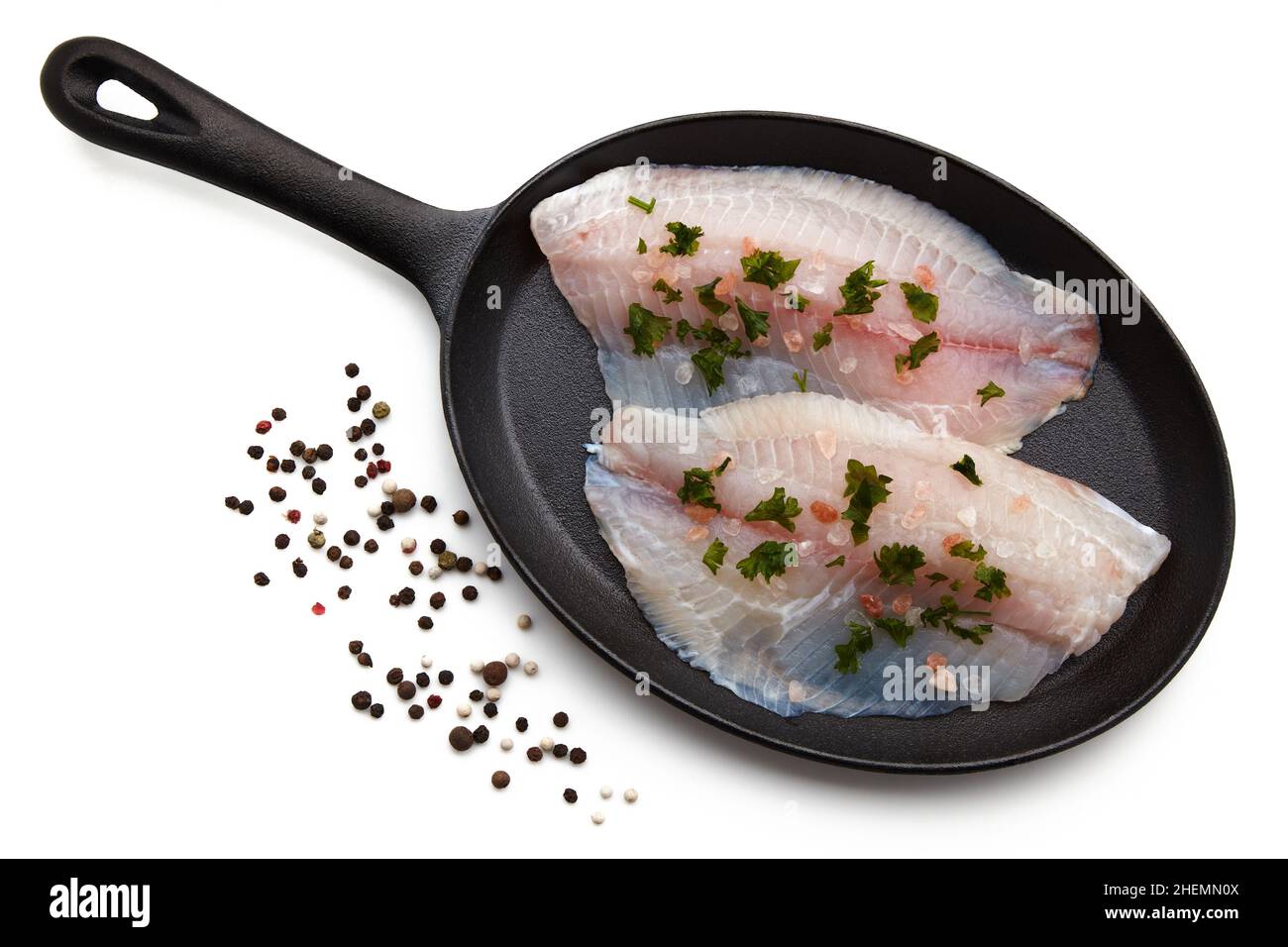 Weißes Fischfilet, das mit Salz und gehackter Petersilie verschüttet wurde, liegt auf einer gusseisernen Pfanne Stockfoto