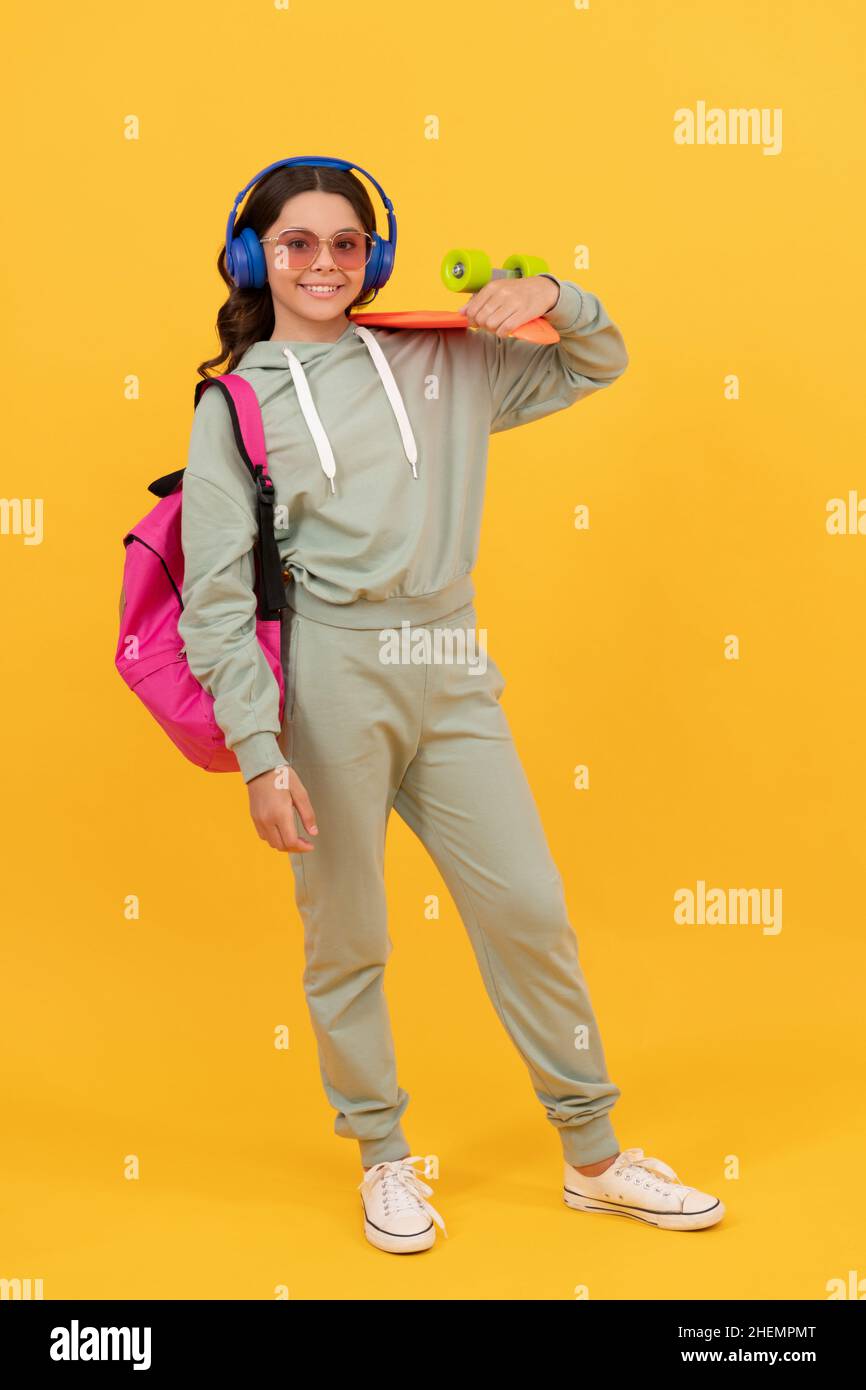 Fröhlicher Teenager in aktivem Ohr, der auf gelbem Hintergrund Pennyboard hält, Board Skating Stockfoto