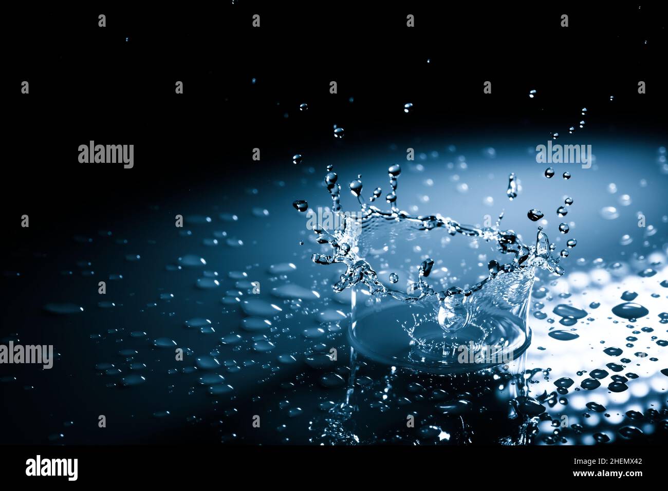 Wunderschöne Spritzkrone aus einem Tropfen Wasser, der auf eine harte Oberfläche fällt. In blauem Licht auf schwarzem Hintergrund Stockfoto