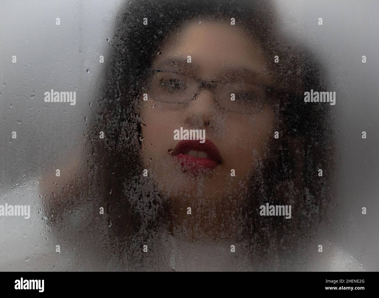 Nahaufnahme einer Frau hinter einem nassen Glas, Fokus auf ihre roten Lippen Stockfoto