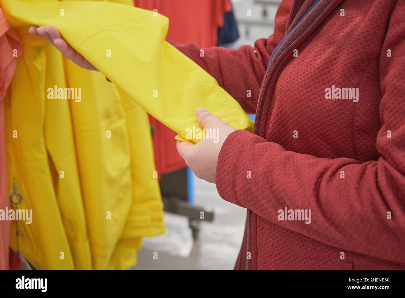 Kaukasische Frau wählt gelben Windbreaker aus dem Regen im Laden zu kaufen Stockfoto