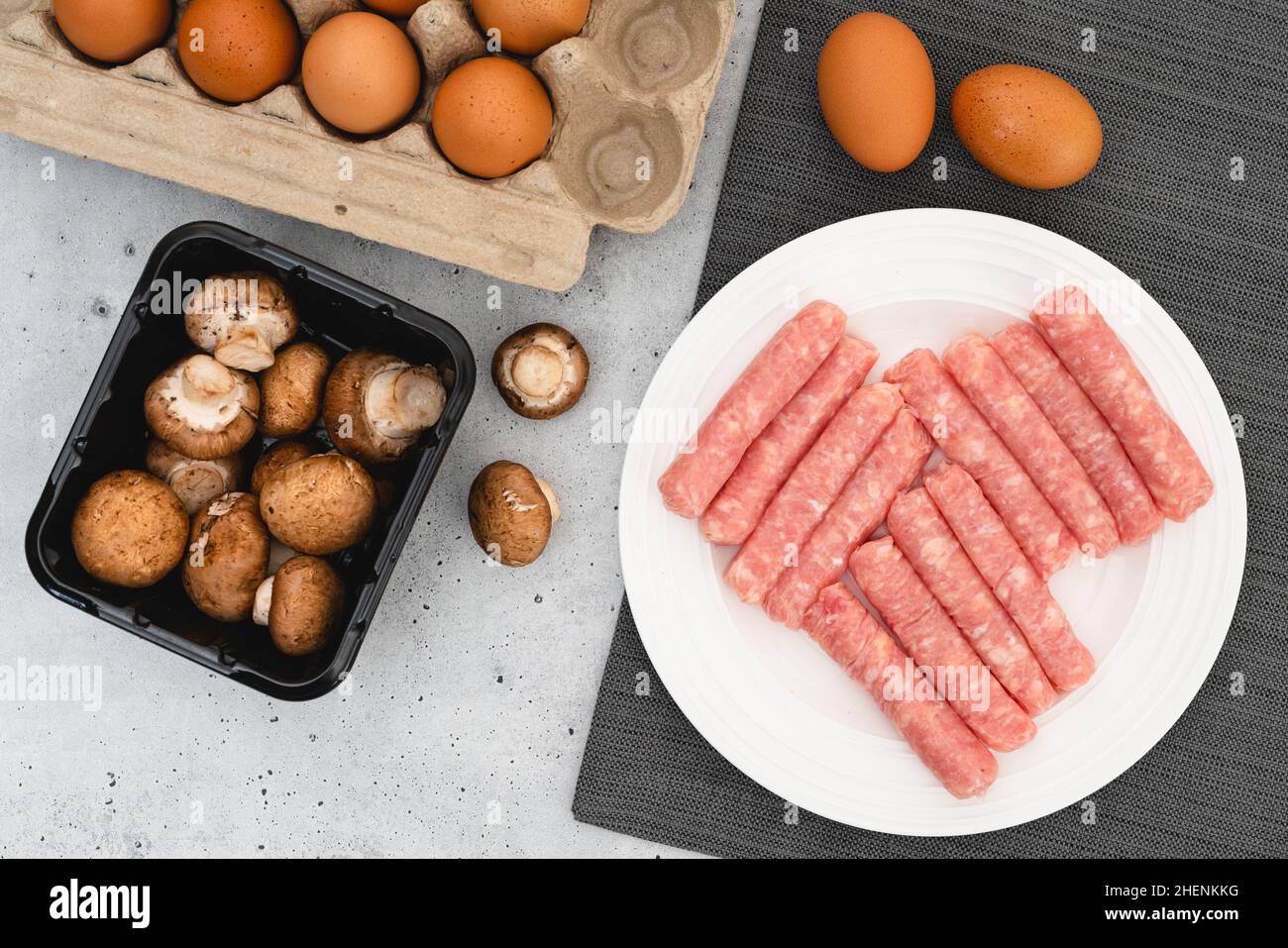 Hähnchenfrühstückswürste, Beby Bella Pilze, Eier, Nahaufnahme, flaches Lay. Rohe Zutaten auf dem Küchentisch Stockfoto