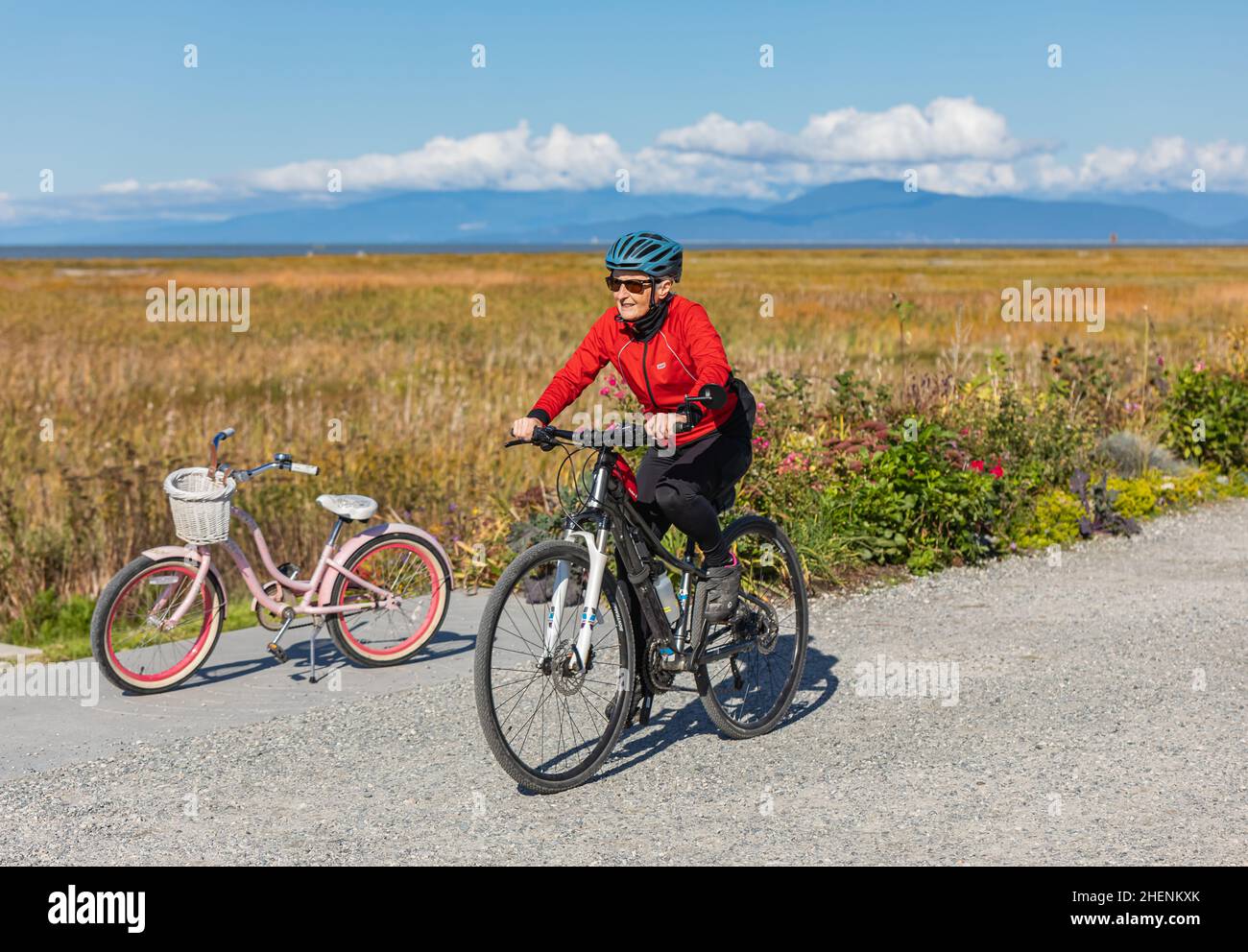 Lächelnd fit ältere Frau auf einem Fahrrad in einem Park. Glückliche ältere Frau mit Helm auf dem Sportfahrrad. Straßenfoto, Reisefoto, Konzeptfoto aktiv Stockfoto