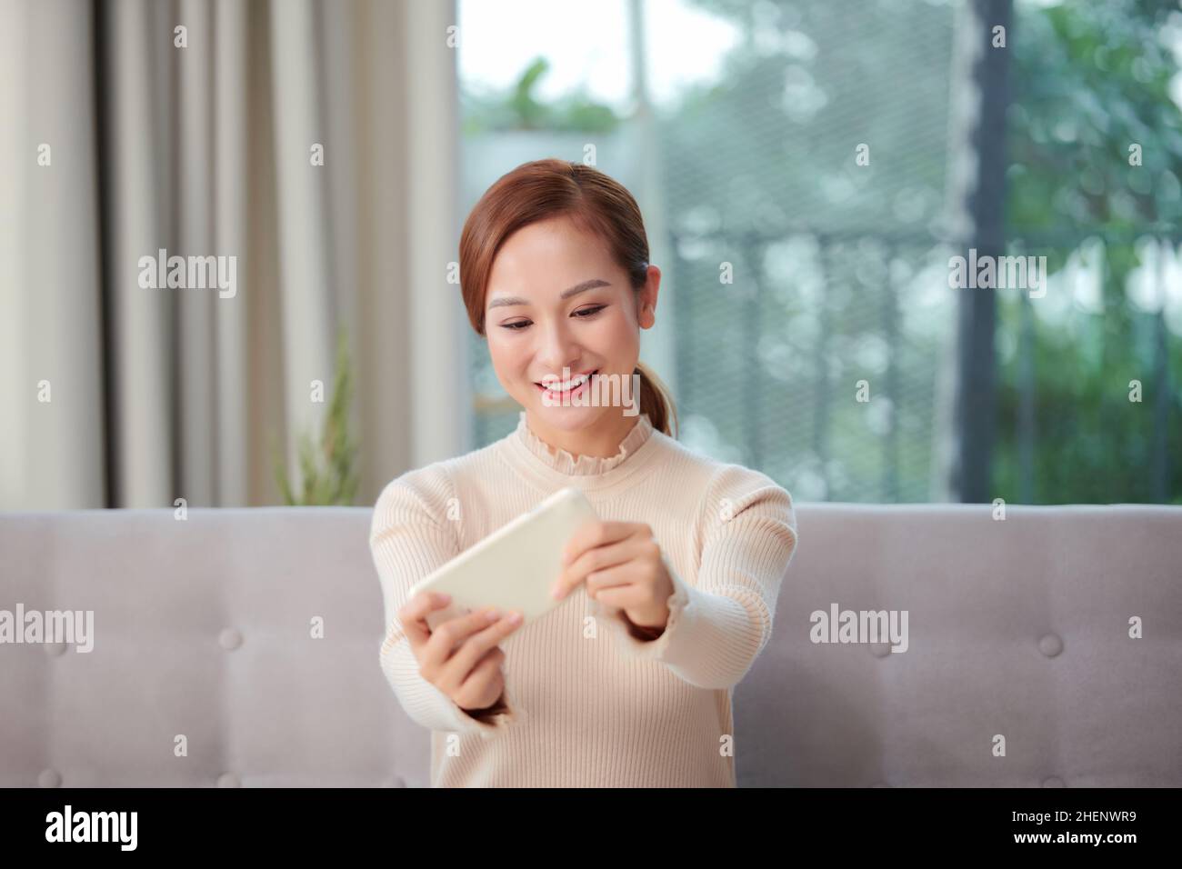 Hübsche Frau spielen Handy-Spiel per Telefon und fühlen sich glücklich Zu Hause Stockfoto