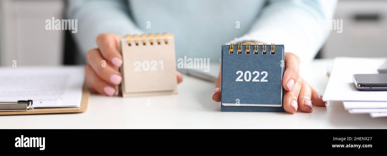 Frau hält Kalender für 2021 und 2022, während sie am Schreibtisch sitzt Stockfoto