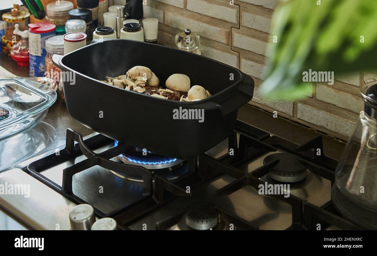 Ein großes Stück Rindfleisch mit Pilzen wird in einem speziellen Kessel auf einem Gasherd gebraten Stockfoto