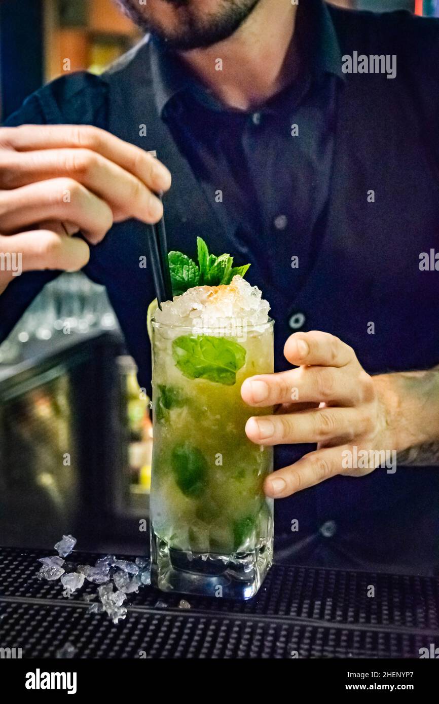 Ein Barkeeper bringt den letzten Schliff zu einem leckeren frisch zubereiteten Mojito-Cocktail, indem er Trinkhalme hinzufügt Stockfoto