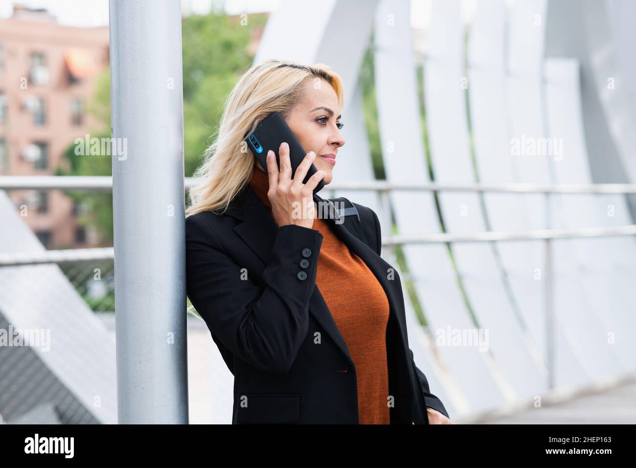 Frau in formeller Kleidung, die sich auf einen Posten lehnt, während sie mit dem Mobiltelefon auf der Straße spricht Stockfoto
