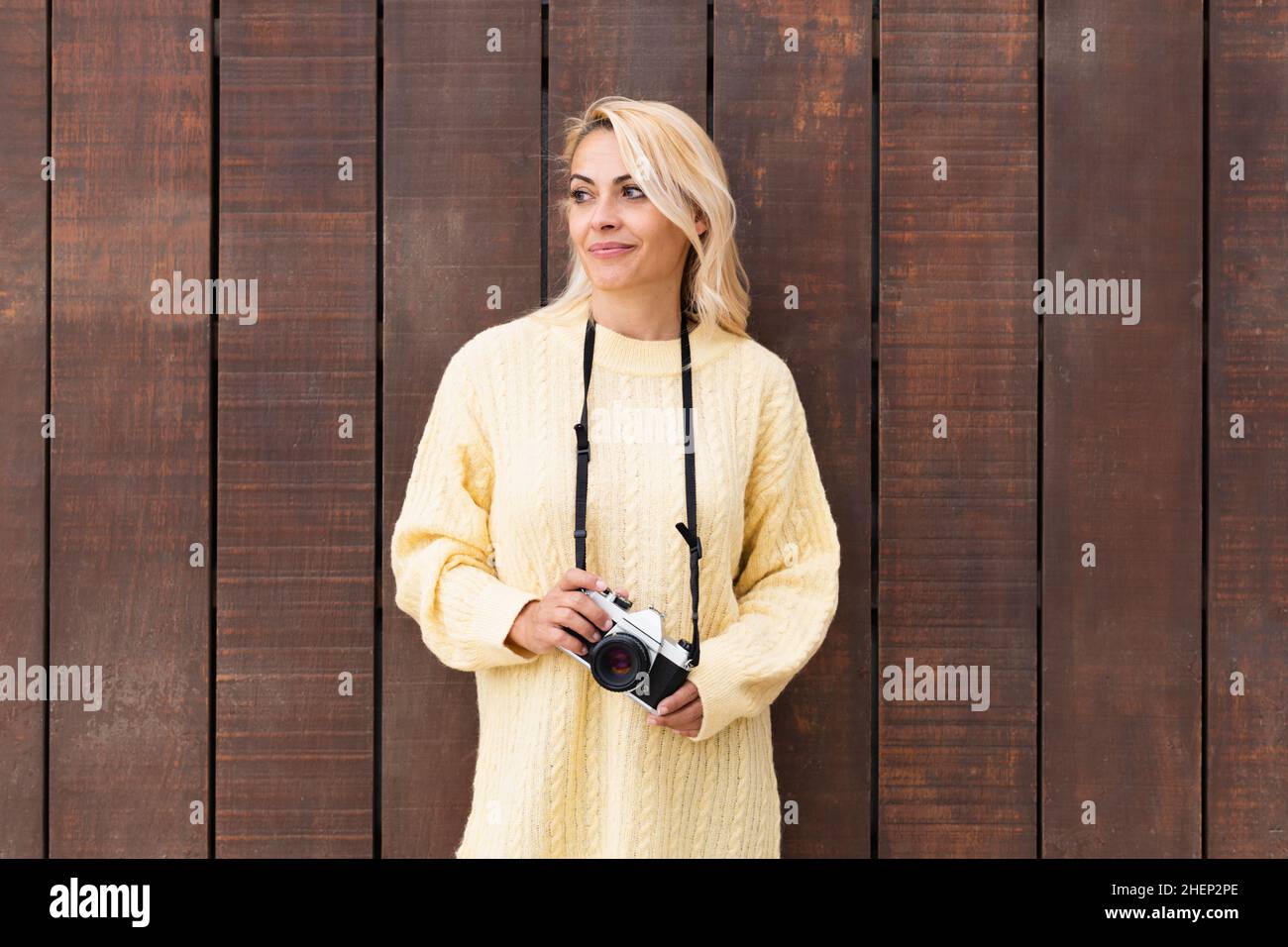 Frau, die eine Kamera hält, während sie sich an eine Holzwand lehnt Stockfoto