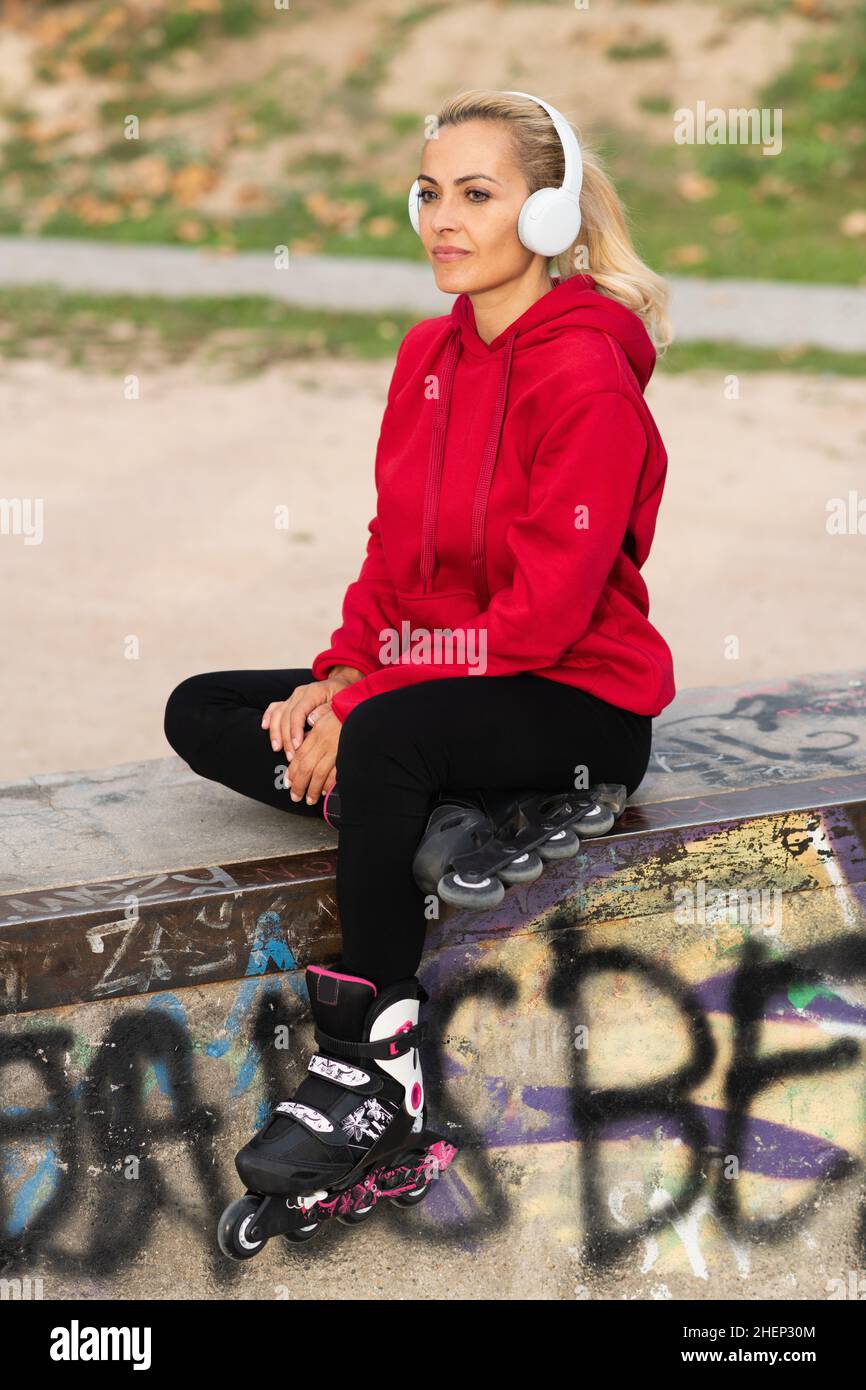 Vertikales Foto einer Frau, die im Skatepark mit Kopfhörern Musik hört Stockfoto