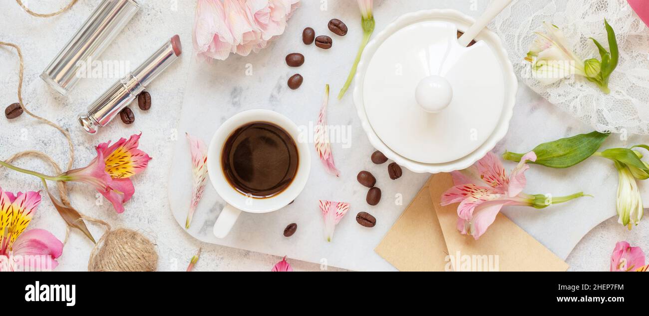 Kaffeetasse in der Nähe von rosa Blumen, Lippenstift und Umschlag auf weißem Tisch Draufsicht. Romantisches Frühstück Stockfoto