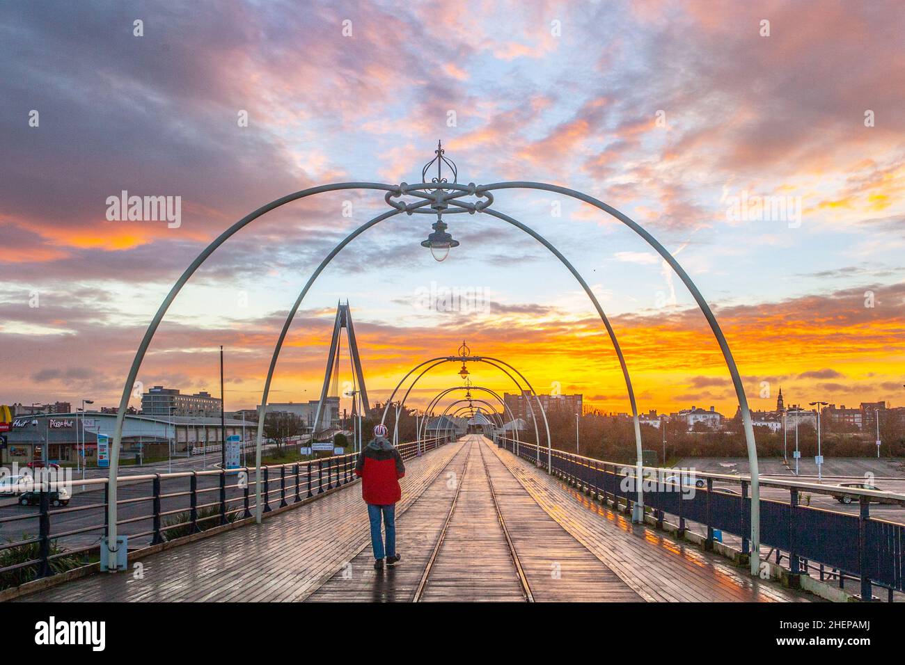 Sonnenaufgang in Southport, Merseyside. Wetter in Großbritannien Januar 2022. Spaziergänger am Pier machen einen Spaziergang an einem milden Januarmorgen, nachdem der Regen über Nacht nachgelassen hat. Der alte, aber restaurierte Southport Pier ist der älteste eiserne Pier des Landes, der seit über 150 Jahren an der Küste steht. Es wird erwartet, dass es ein trockener Tag mit vielen Sonnenstrahlen und nur ein paar Wolken wird. Stockfoto