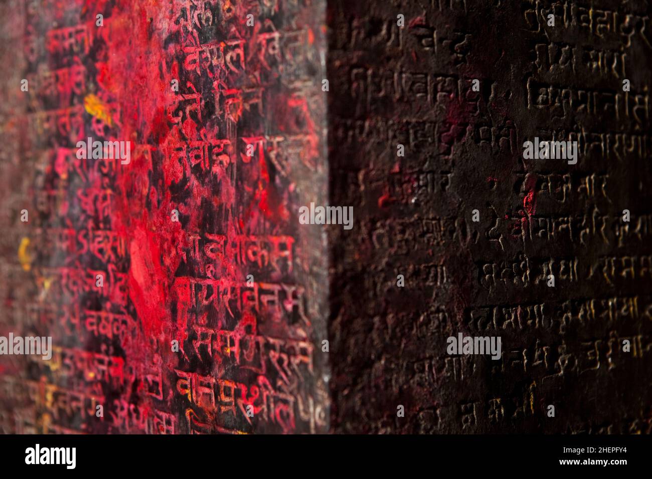 Hinduistischer religiöser Stein, der mit sanskrit geschnitzt und mit Opfergaben an einem Gebetsort in Bhaktapur während des nepalesischen Neujahrs rot beschmiert wurde. Stockfoto