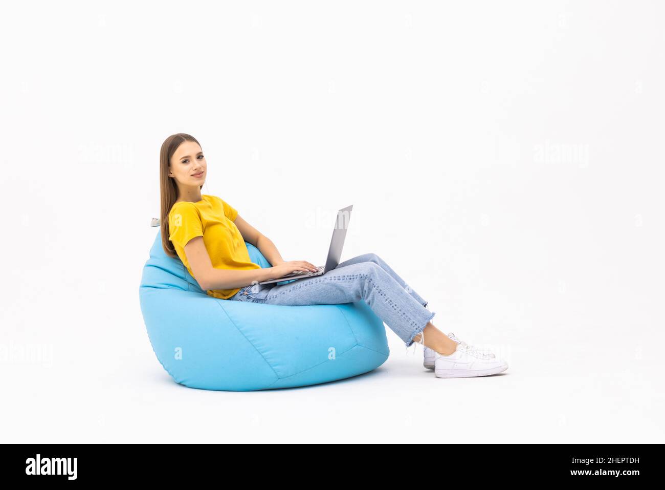Junge Frau arbeitet an ihrem Computer Chat mit Start-up-Kunden sitzen große Tasche Lounge Stuhl tragen lässige Kleidung über weißen Hintergrund Stockfoto