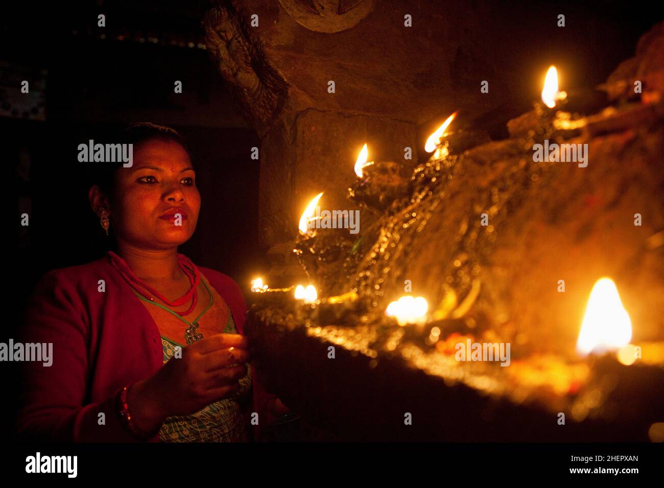 Einheimische Newari-Frau, die während der nepalesischen Neujahrsfeierlichkeiten (Bisket Jatra) in Bhaktapur Puja (Gebet/Opfergabe) an einem mit Kerzen angezündeten Hindu-Schrein macht. Stockfoto