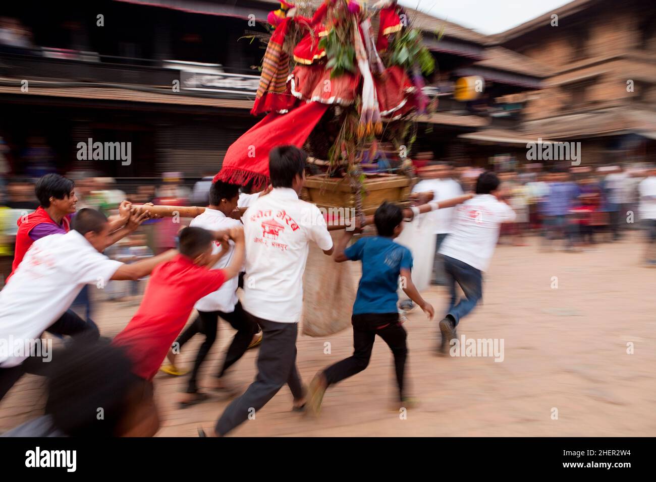 Jugendliche, die während der nepalesischen Neujahrsfeierlichkeiten (Bisket Jatra) im UNESCO-Weltkulturerbe Bhaktapur einen Khat (Palanquin) durch die Straße tragen. Stockfoto
