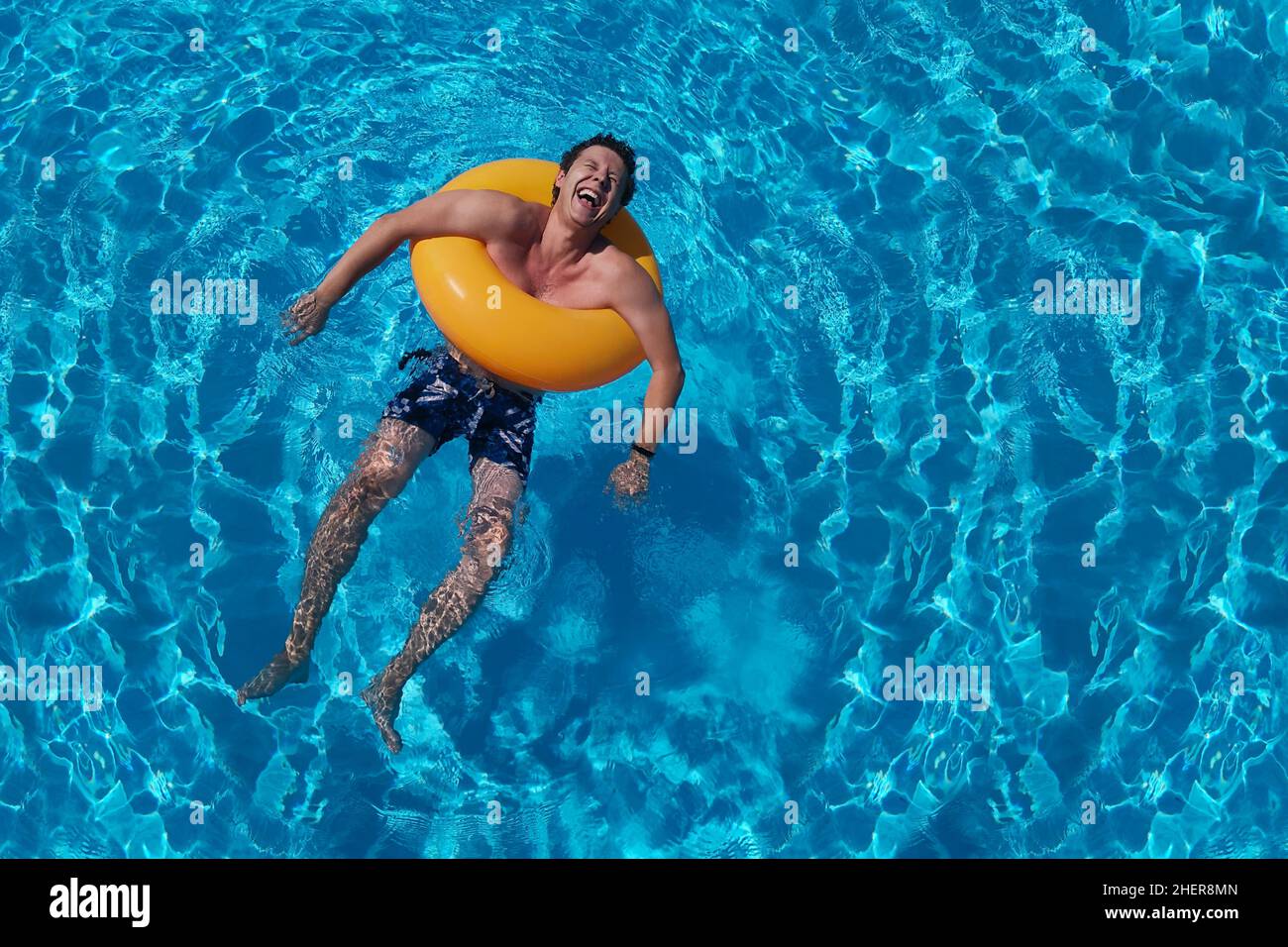 Orangefarbener Kreis und lachender Kerl im Sommerpool. Sattblauer Wasserhintergrund. Sommerferien, Lachen, Lebensfreude und fröhlicher Mann. Poolparty Stockfoto