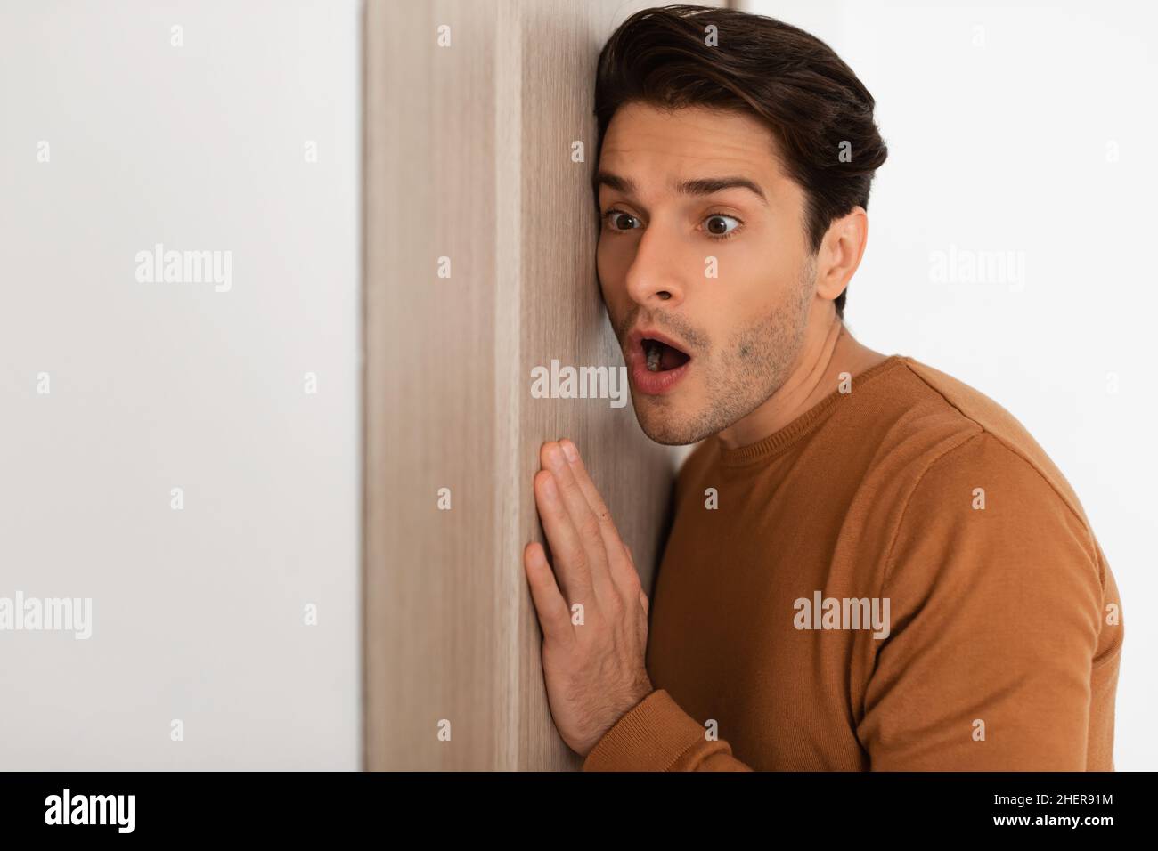 Schockierter junger Mann, der durch die Tür zuhörte Stockfoto