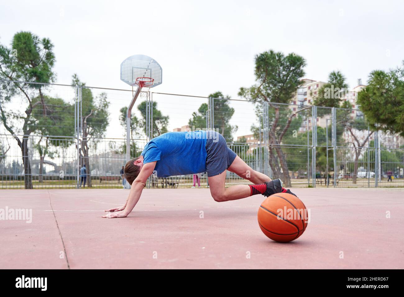 Seitenansicht eines sportlichen, jungen Mannes, der Liegestütze mit einem Basketball-Workout im Freien auf dem Basketballplatz macht. Horizontale Aufnahme. Stockfoto