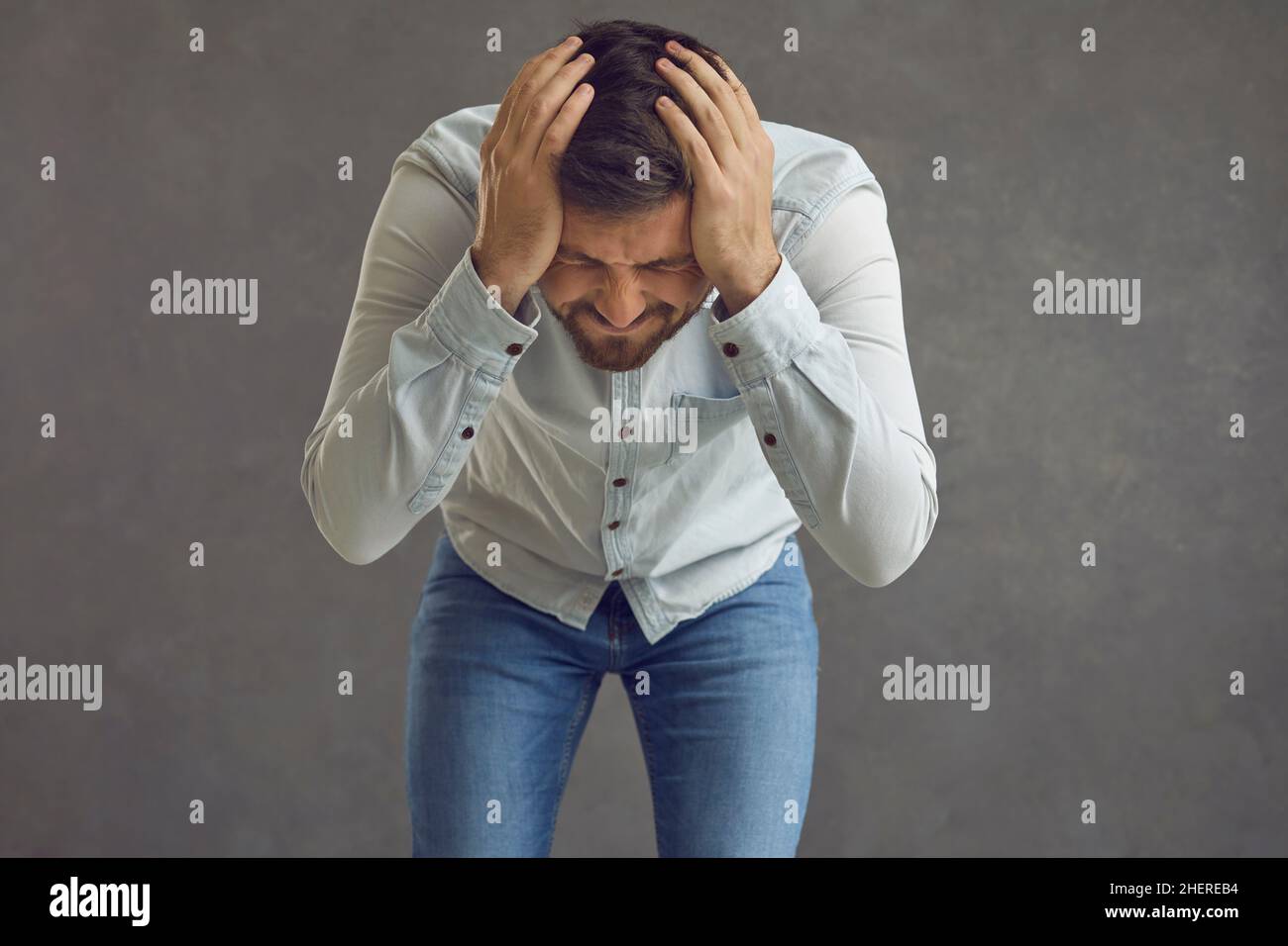 Verärgert frustrierter Mann, der verzweifelt seinen Kopf vor grauem Studiohintergrund hält Stockfoto