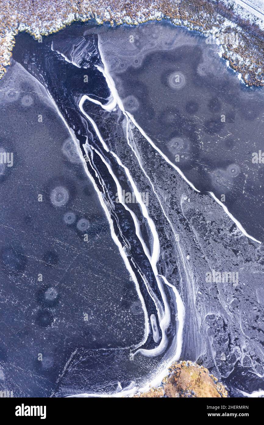 Luftaufnahme auf einem gefrorenen Teich, der mit Eis bedeckt ist und riesige Risse und Muster aufweist Stockfoto