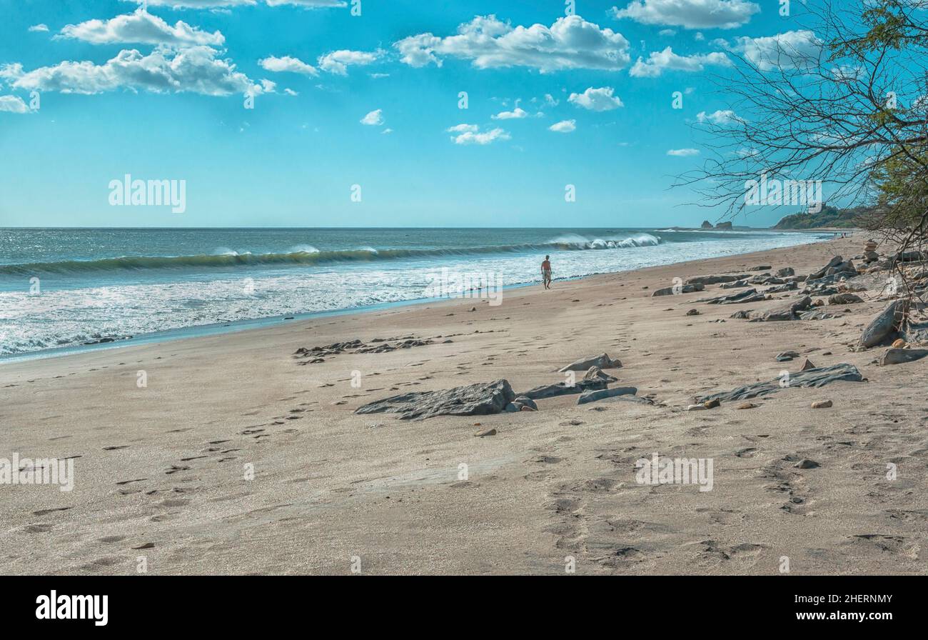 Ein Mann, der in der Nähe des Strandes mit Wellen unterwegs war Ufer und Felsen im Hintergrund an einem sonnigen Tag Stockfoto
