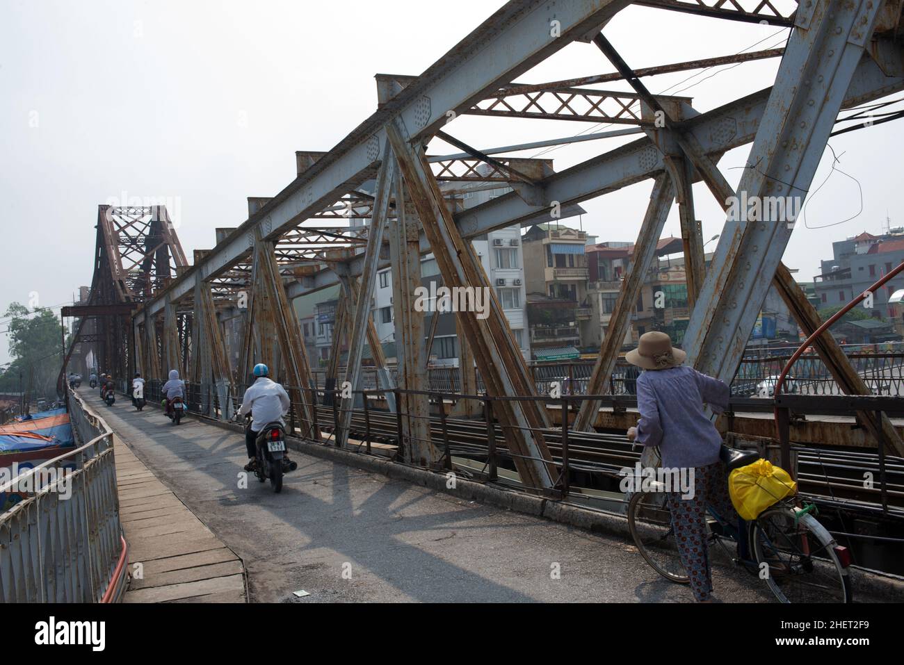 Nicht erkennbare Menschen, die von ihrem Rücken aus die alte Brücke mit dem Fahrrad oder dem Motorrad überquerten. Brücke über den Fluss in Hue, Vietnam, Asien Stockfoto