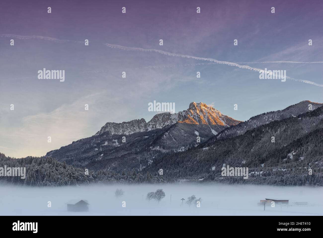 Farbenprächtiger Himmel bei Sonnenaufgang mit riesigen Bergen und nebliger Wiese Stockfoto