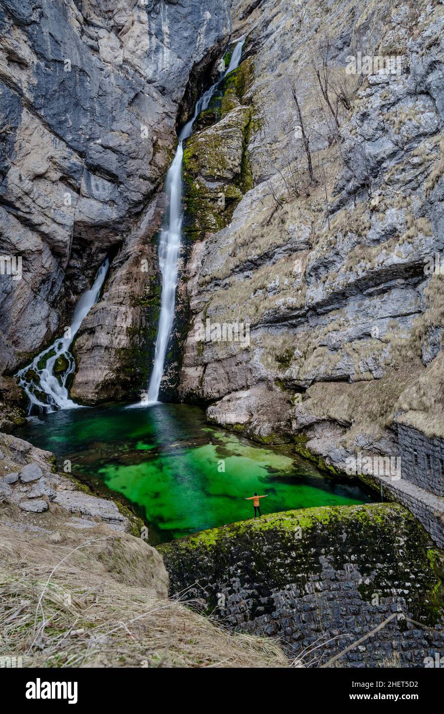 Eine Person mit gelber Jacke, die am Rande des Savica-Wasserfalls in Slowenien, des Bohinj-Sees und des Triglav-Nationalparks steht Stockfoto