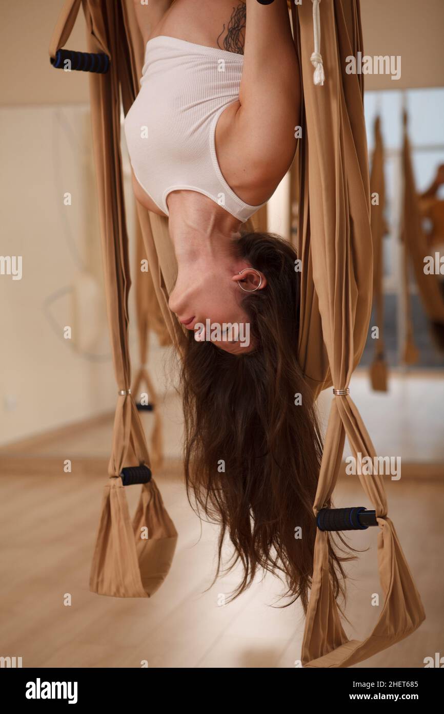 Vertikale geschnittene Aufnahme einer langhaarigen schönen Frau, die im Fitnessstudio an einer Yoga-Hängematte arbeitet Stockfoto