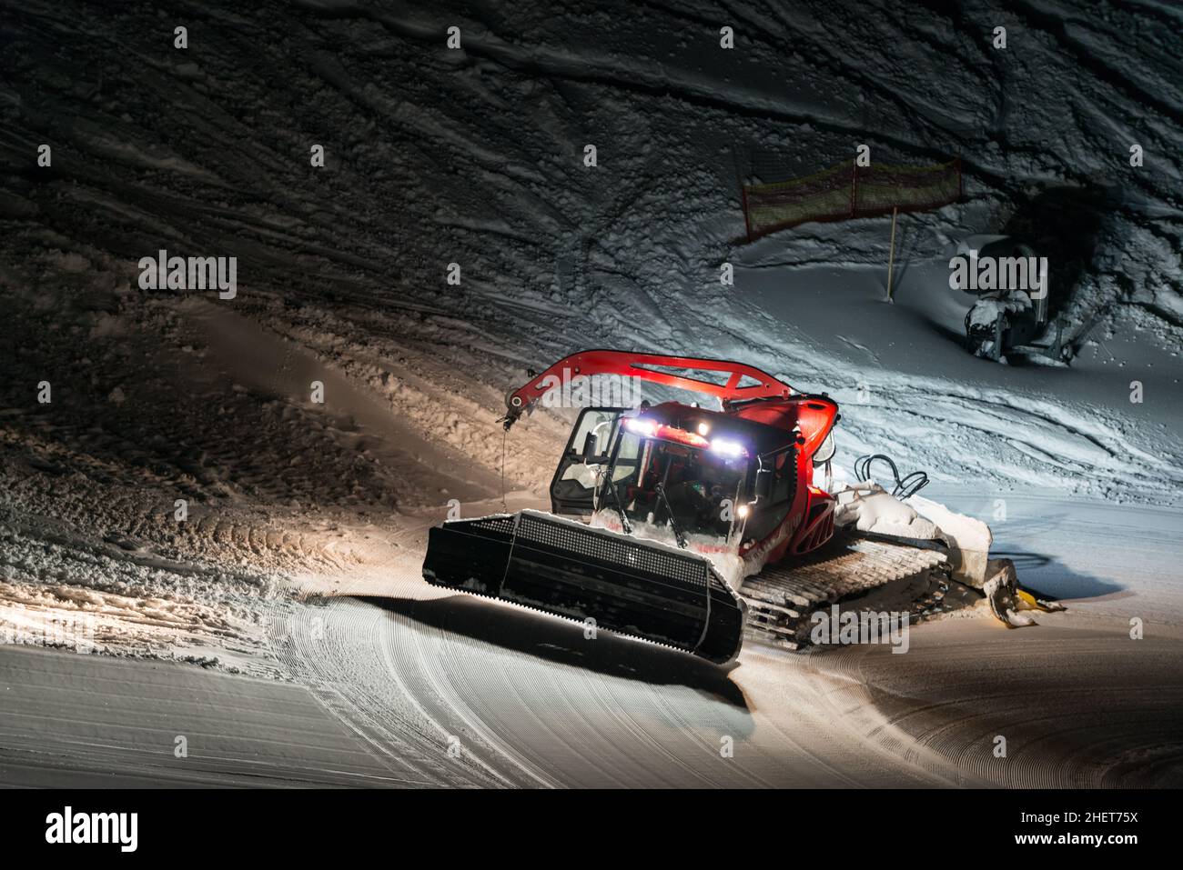 Nachtaufnahme des roten Pistenraupe bei der Arbeit in österreich Stockfoto