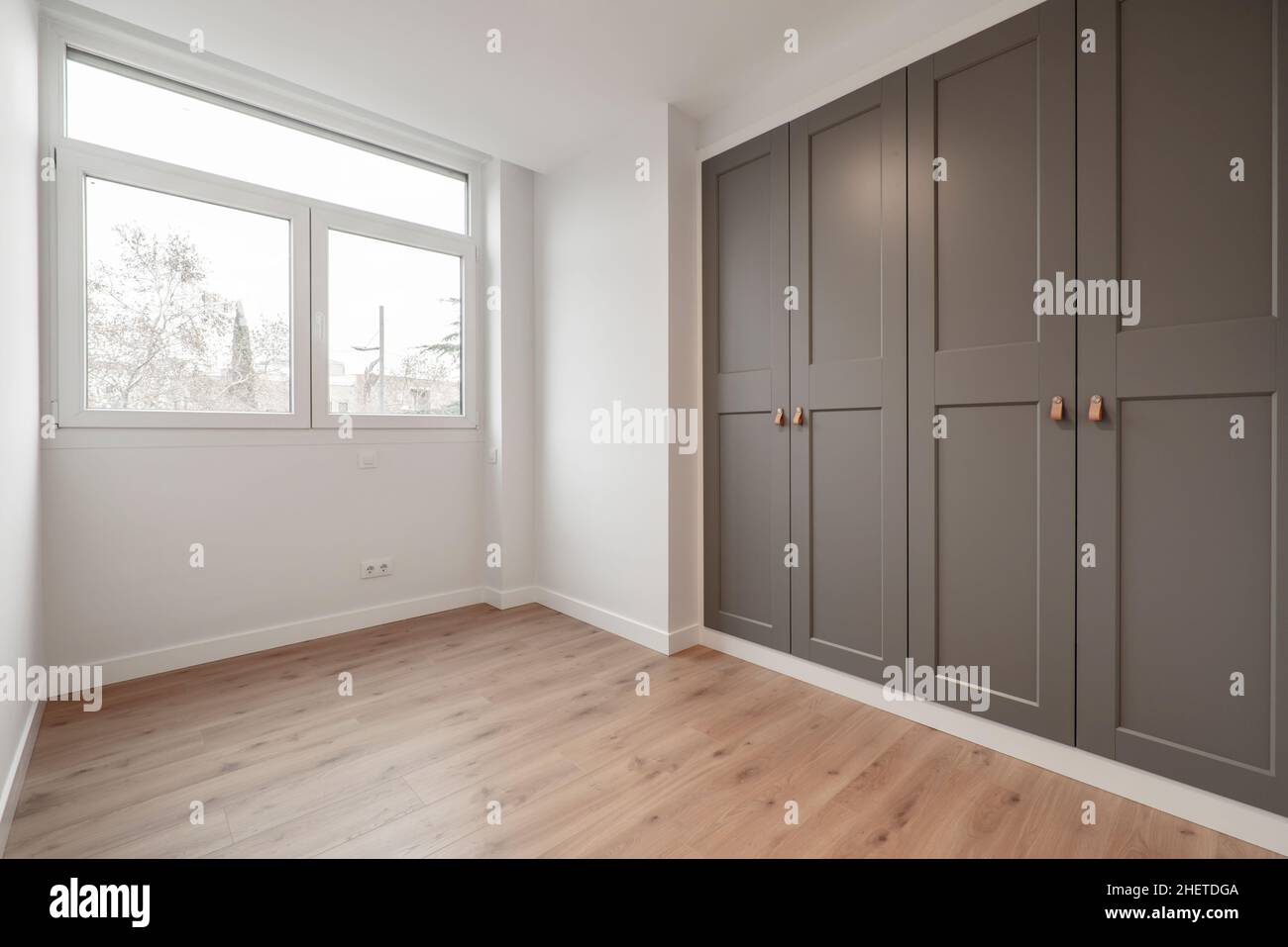 Schönes Zimmer mit großem Fenster, Kiefernholzböden und Einbauschränken mit grauen Türen Stockfoto