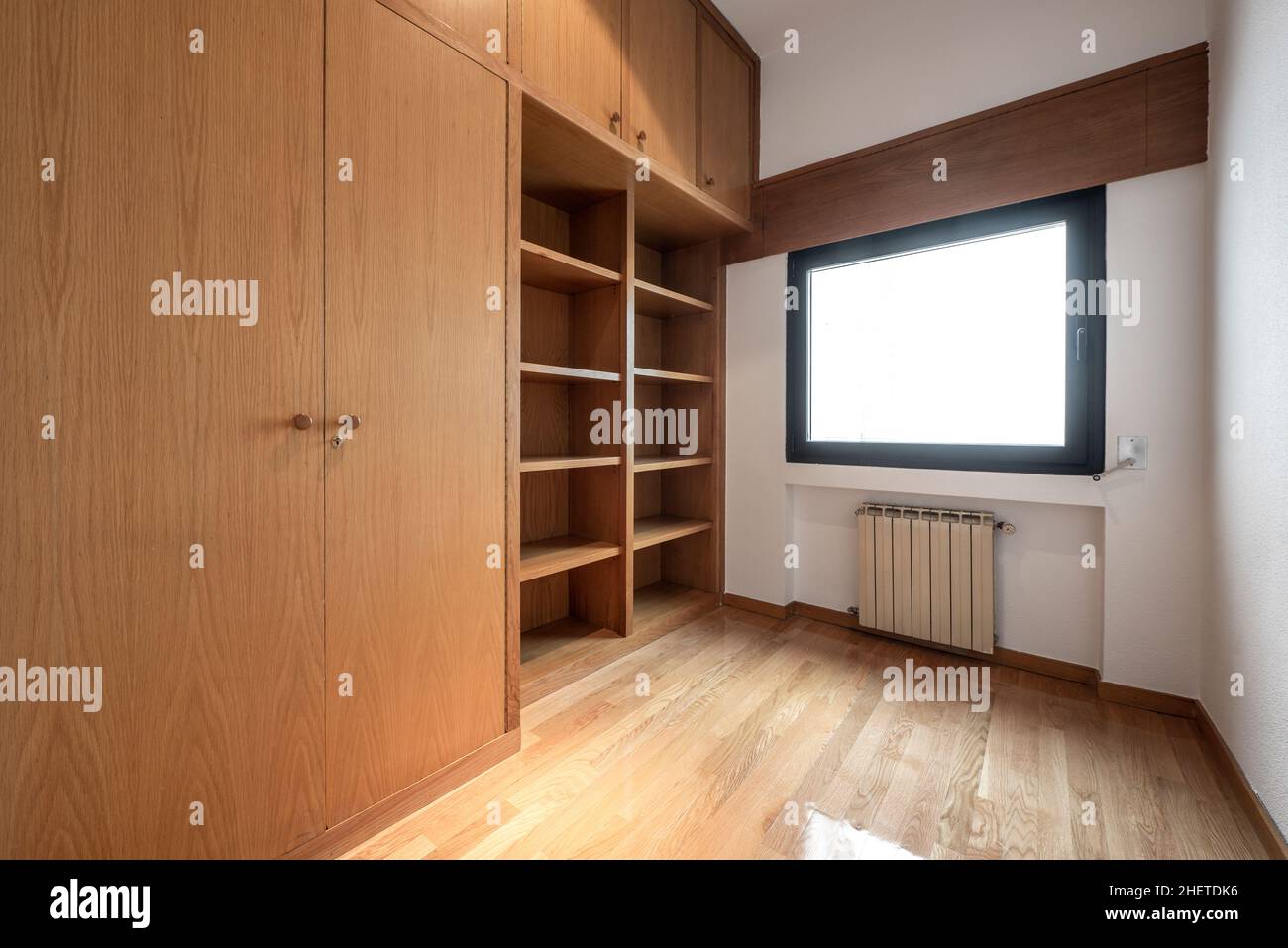 Leeres Zimmer mit eingebautem Eichenschrank und Bücherregal, Eichenparkettboden und Aluminiumheizkörper unter dem Fenster Stockfoto
