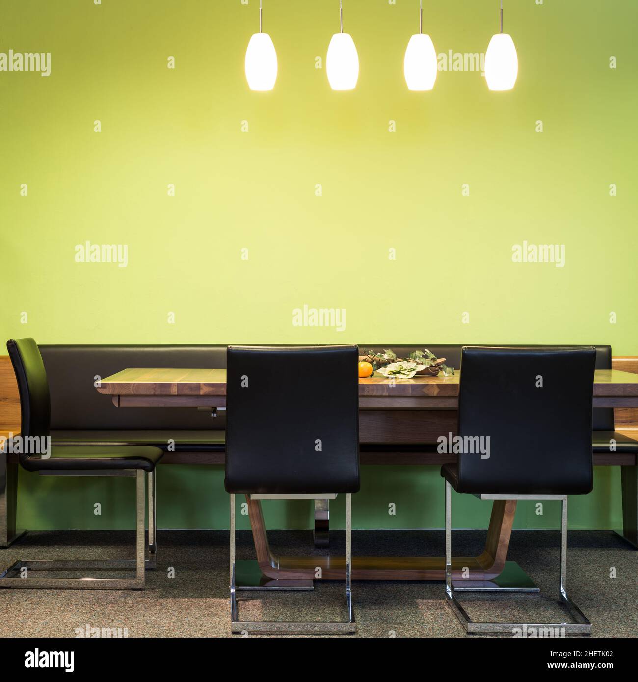 Freischwellige Stühle am Holztisch mit Lampen und grüner Wand Stockfoto