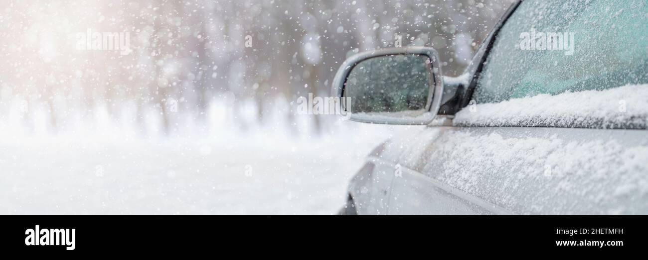 Das Auto fährt durch den Schnee, die helle Wintersonne scheint vor dem Hintergrund des Waldes. Rückspiegel in Nahaufnahme. Das Fahrzeug ist abgedeckt Stockfoto