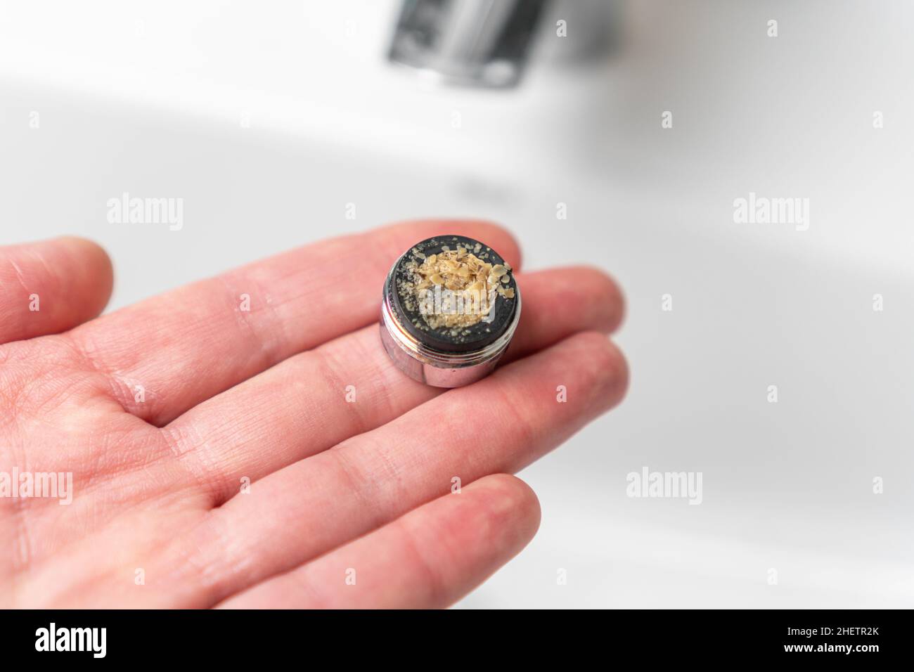 Schmutziger Wasserfilter in der Hand über dem Wasserhahn im Waschbecken. Verstopfte Belüftungsanlage im Bad. Wartung von Sanitäranlagen. Calciumschlacke Stockfoto