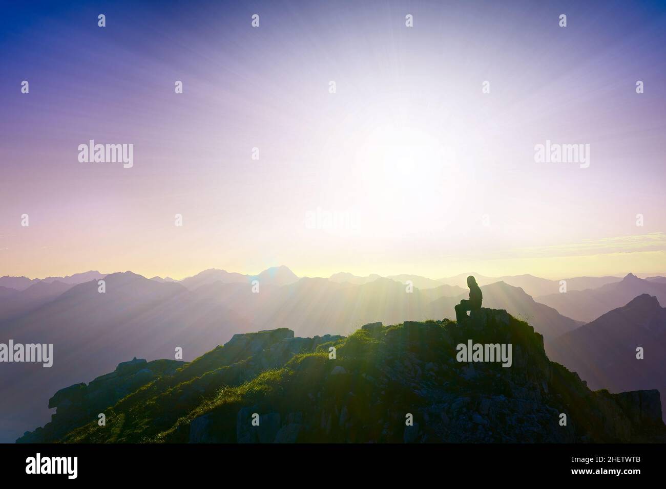 Einsames trauriges Mädchen, das auf dem Berggipfel sitzt und über die alpen blickt Stockfoto
