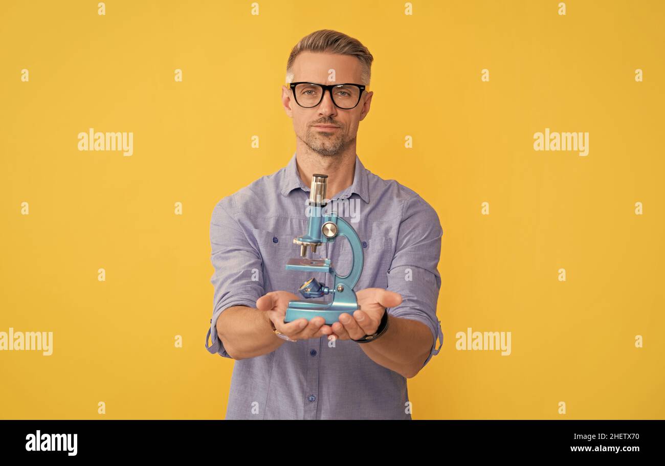 Mann in einer Brille hält Mikroskop auf gelbem Hintergrund, Data Science Stockfoto