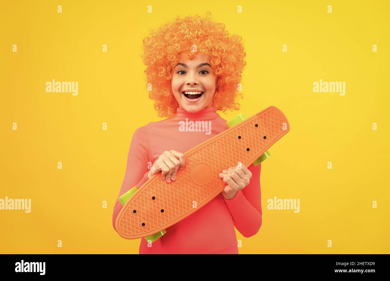 Happy cool Mädchen mit orangefarbenen Haaren in rosa Poloneck Lächeln hält Pennyboard, Skateboard Stockfoto
