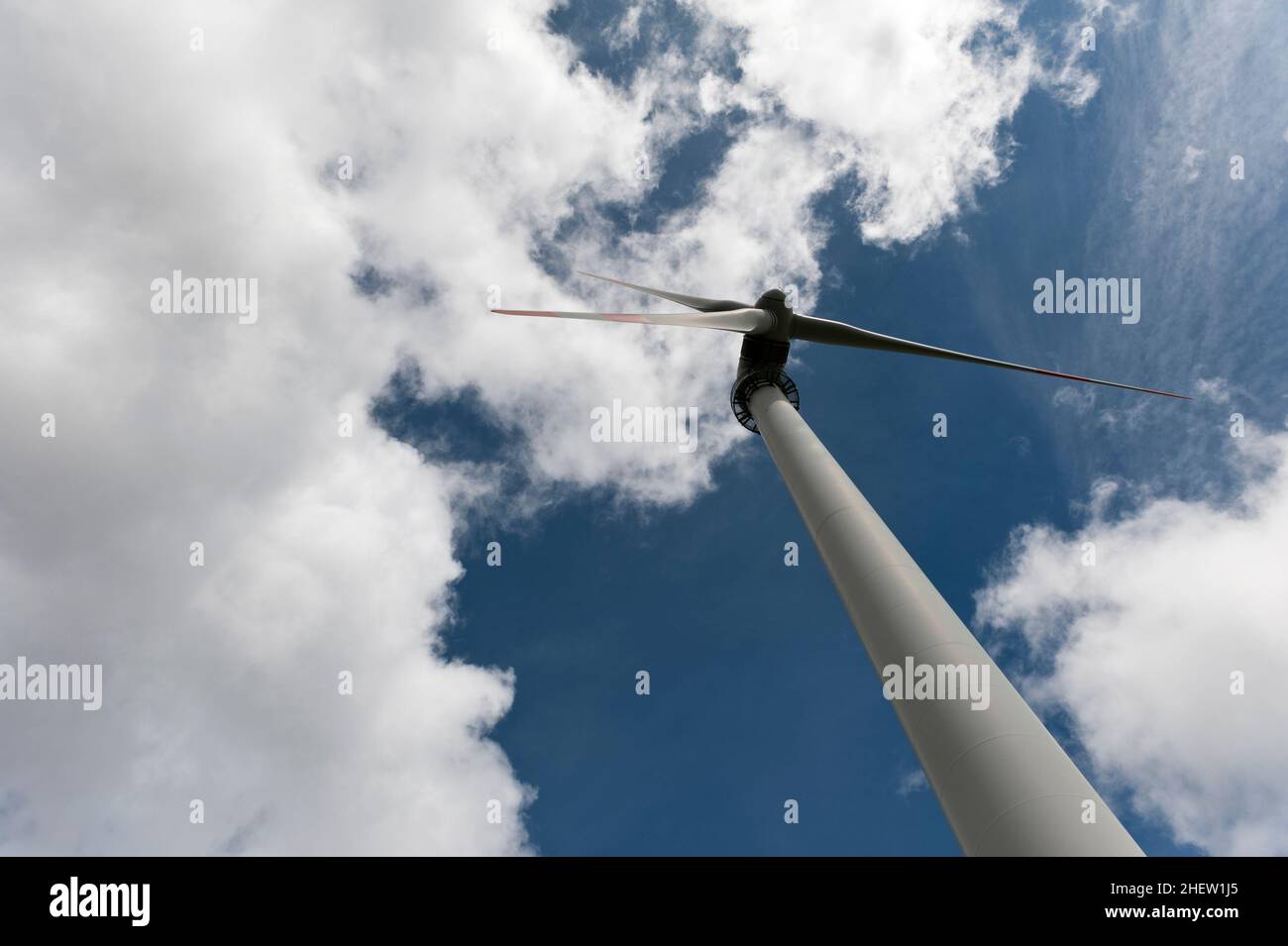 Riesige Windkraftanlage oder Motor mit drei großen Flügeln auf tiefblauem bewölktem Himmel Stockfoto