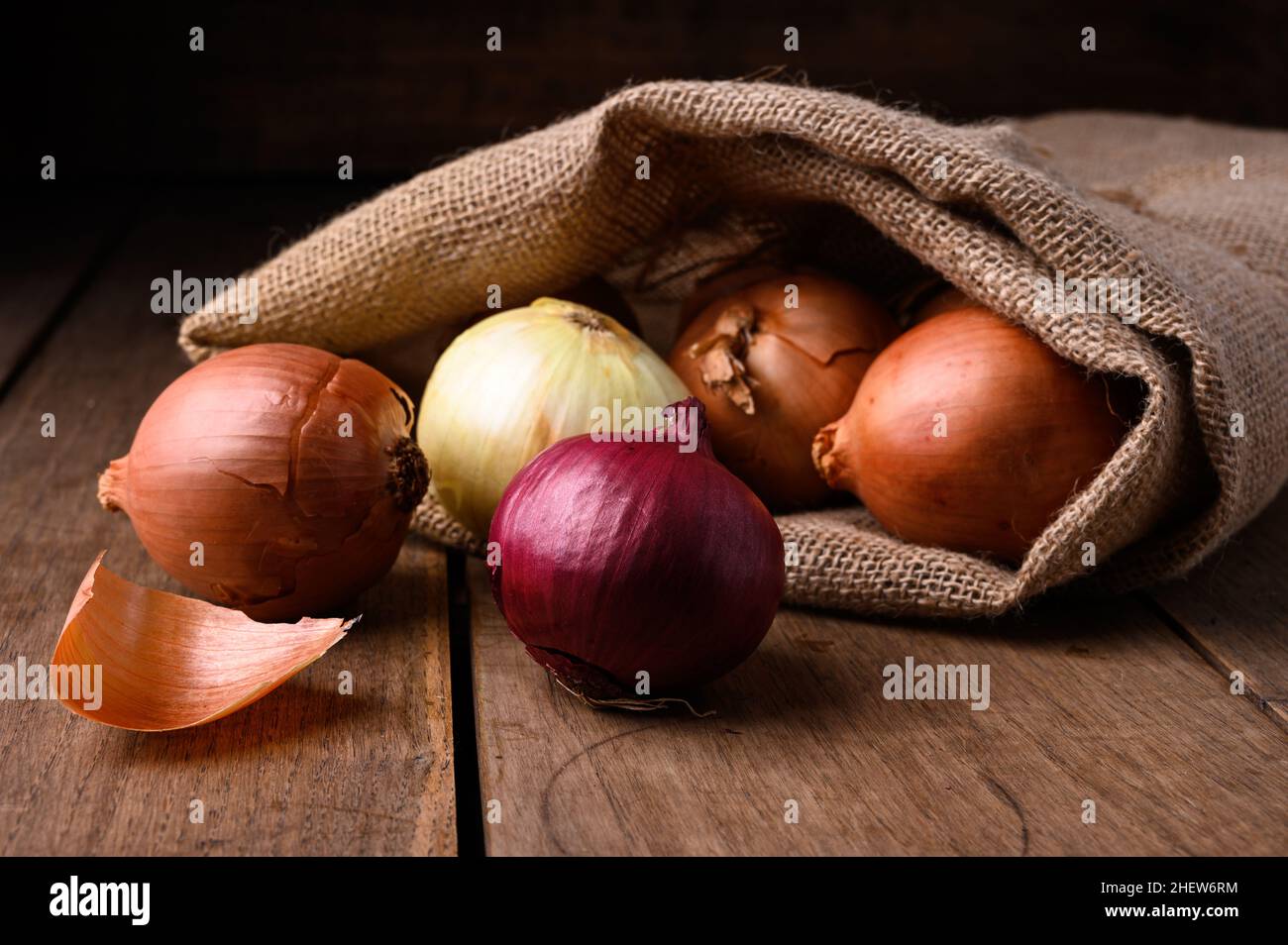 Rote und weiße Zwiebeln auf einem rustikalen Holztisch, die aus einem Stoffsack in der Küche auslaufen, Draufsicht. Hochwertige Fotos Stockfoto