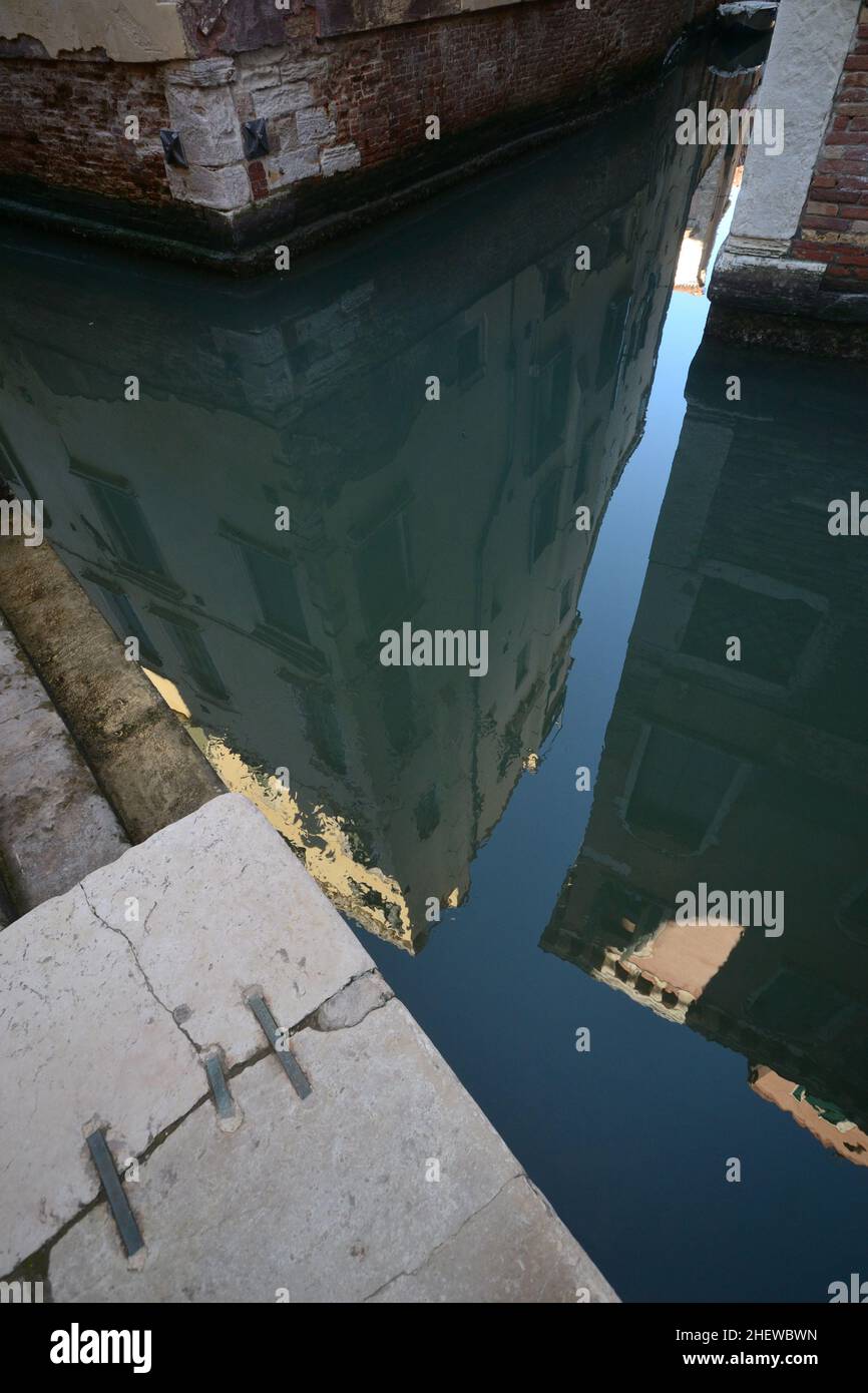 Ungewöhnlicher urbaner Blick auf venedig. Wohngebäude mit teilweise abgenommenem Putz sind Reflexionen auf der wässrigen Oberfläche eines Kanals zu sehen Stockfoto