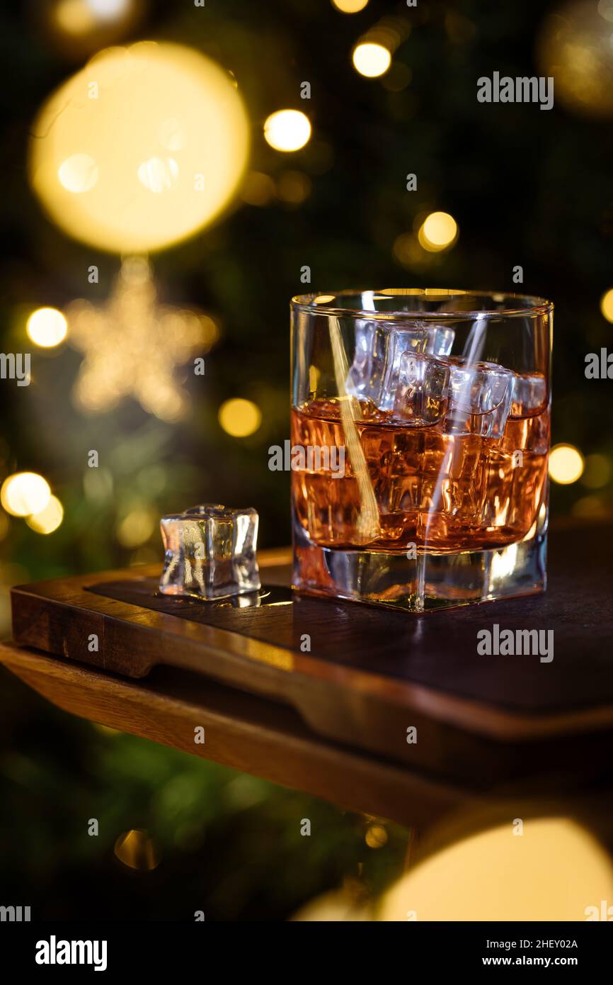 Glas Whiskey oder aperol Spritz mit Eiswürfeln in festlicher Weihnachtsstimmung mit Weihnachtsbaum im Hintergrund Stockfoto