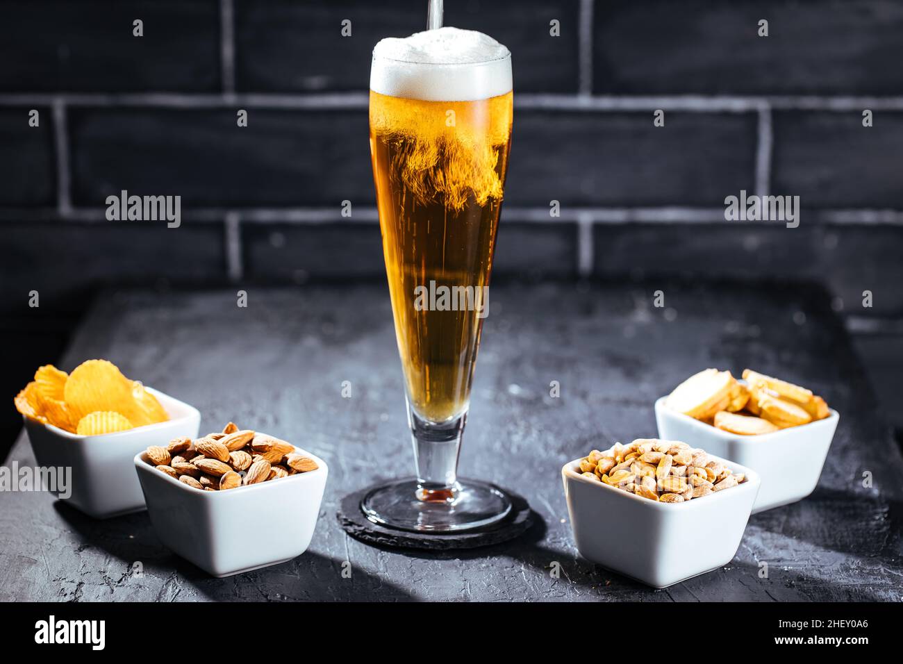 Ein Glas Bier mit Schaum und vier verschiedene Snacks Stockfoto