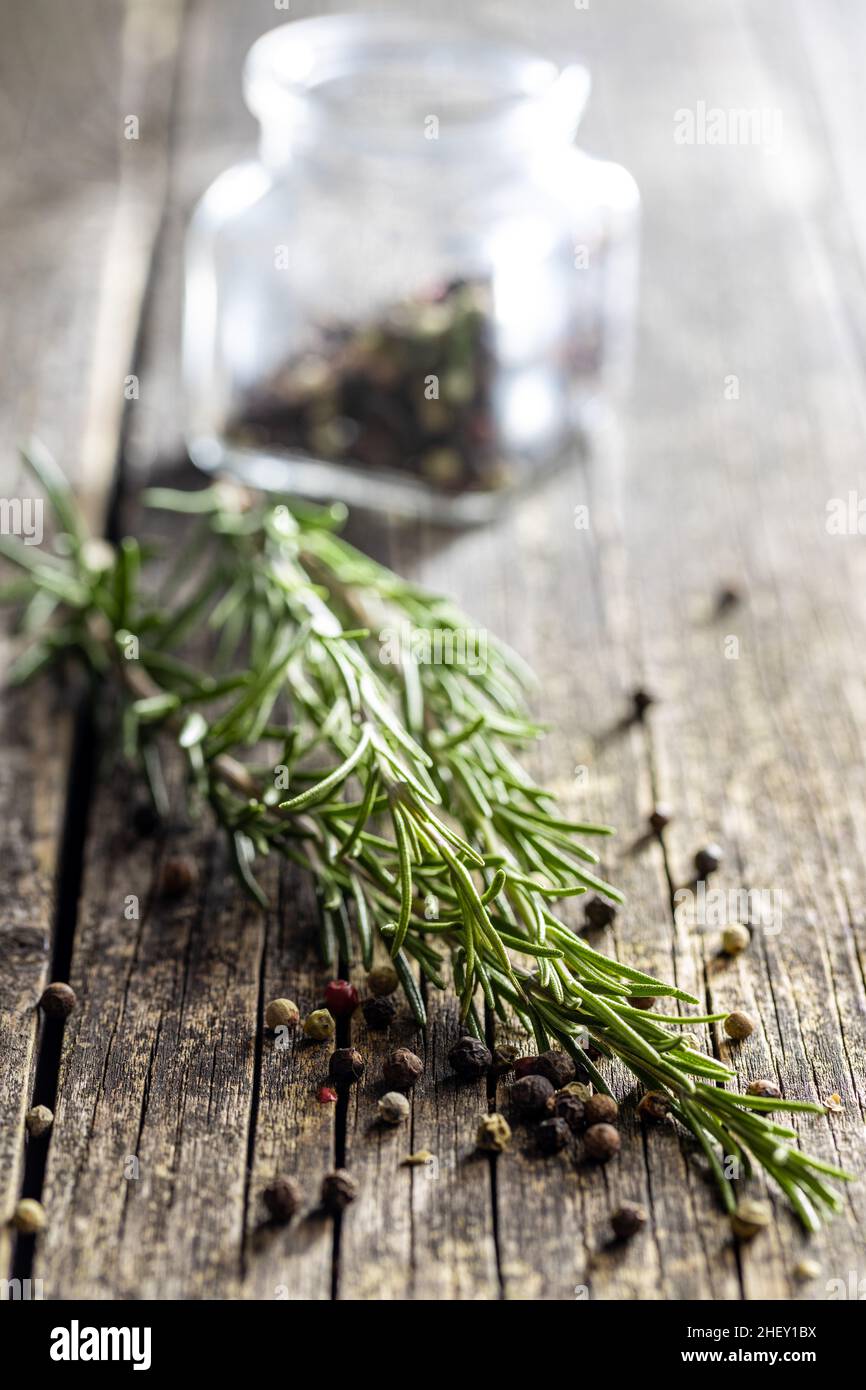 Grüner Rosmarinzweig und ganze Pfefferwürze auf Holztisch. Stockfoto