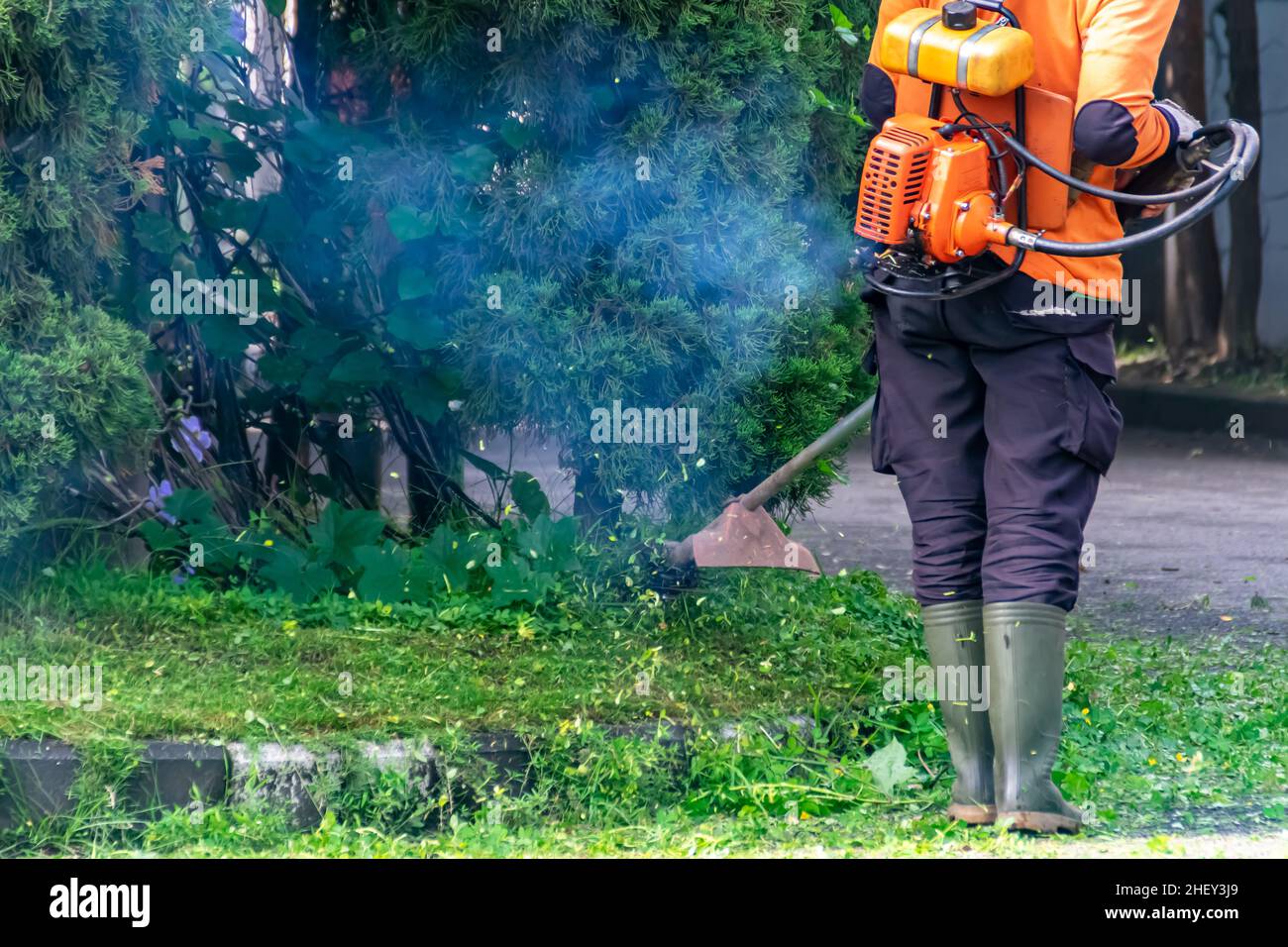 Ein öffentlicher Arbeiter säuberte den Stadtstraßenhof mit dem Grasschneider oder der Trimmermaschine mit einer Rauchblase Stockfoto
